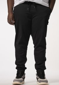Zwarte tapered joggerbroek met een trekkoord in de taille, zijzakken en elastische boorden, gecombineerd met grijze en zwarte sportschoenen.