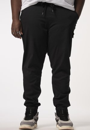 Zwarte tapered joggerbroek met een trekkoord in de taille, zijzakken en elastische boorden, gecombineerd met grijze en zwarte sportschoenen.