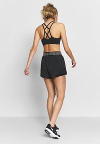 Svart sport-bh med korsade bakre band, kombinerad med svarta shorts med randigt elastiskt midjeband och svarta träningsskor.