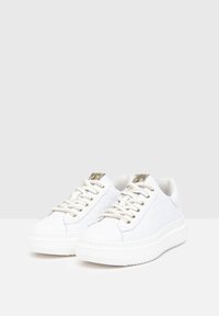 Weiße Sneaker mit einem glatten Lederoberteil, strukturierten Details, goldfarbenen Ösen und dicken weißen Sohlen für ein minimalistisches Design.