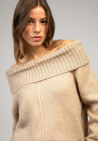 Pull beigne à épaules dénudées avec un col en côte texturé, en matière tricot douce et à coupe ample. Présente un détail en tricot à câble central.