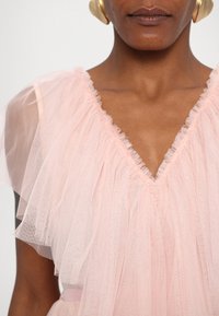 Rochie din tulle roz, cu decolteu în V, mâneci fluture stratificate și finisaj texturat. Design minimalist cu un aspect moale și translucid.