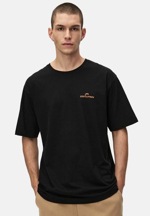 Czarna bawełniana koszulka z okrągłym dekoltem i luźnym krojem. Posiada małe pomarańczowe logo "COALITION" na lewej piersi.