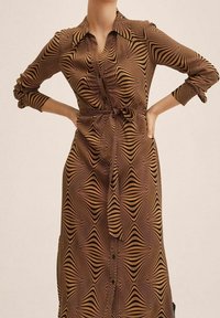 Robe chemise marron à manches longues avec un motif de vagues rayées. Comprend un col à revers, des fermetures à boutons et une taille nouée pour un ajustement modulable.