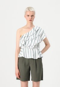 Top cu un umăr, realizat din material alb cu dungi verticale verzi și volănașe stratificate. Asortat cu pantaloni scurți de culoare verde măslinie, creând un efect de peplum.