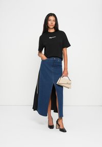 Černé oversized tričko, džínová sukně po kolena s předním rozparkem, černé boty na vysokém podpatku a béžová kabelka s tenkým popruhem.