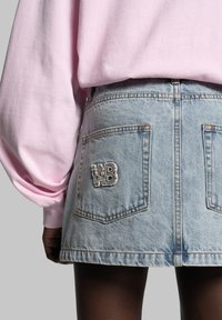 Gonna mini in denim blu chiaro con orlo sfilacciato, dotata di due tasche posteriori e logo "WB" ricamato in filo beige. Abbinata a un top a maniche lunghe rosa.