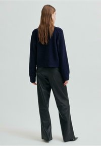 Marineblå strikkegenser med en kort design, kombinert med svarte skinnbukser med rette ben, som har en jevn tekstur og minimal detaljering.