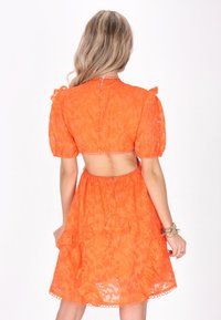 Rochie scurtă cu mâneci scurte, de culoare portocalie, cu un model texturat floral, spate deschis, fustă în straturi și închidere cu buton. Decupajă cu dantelă.