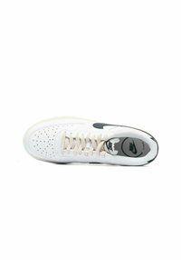 Zapatilla blanca de Nike con puntera perforada, logo negro y cordones crema. Forma redondeada y material texturizado con una suela gruesa.