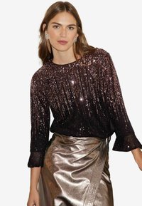Top nero in paillettes con maniche a volant e gonna metallizzata argento lucente, caratterizzata da un design elegante e una texture morbida.