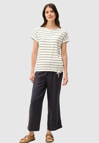 Katoenen gestreept t-shirt in off-white en marineblauw, gecombineerd met losse, donkergrijze broek met een trekkoord in de taille. Platte sandalen.