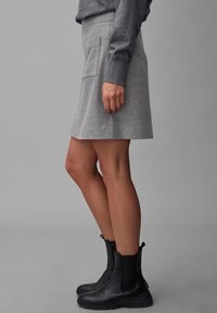 Jupe en laine grise à coupe droite, avec une poche latérale. Associée à des bottines noires, présentant un aspect lisse et texturé.