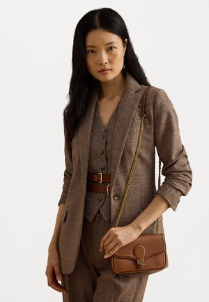 Bruin geblokt tailleurjasje over een bijpassend vest en broek, met een bruin lederen handtas met een gouden kettingstrap en logo-details.