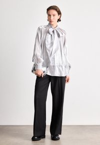 Silver, lightweight blouse with a bow tie, puffed sleeves, and button accents. Paired with black, wide-legged trousers and glossy shoes.