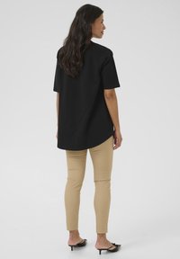 Sort oversized t-shirt med korte ærmer, rundet kant, parret med beige slim-fit bukser og sorte hælhæle. Glat tekstur, afslappet design.