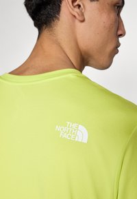 Κοντομάνικο, φωτεινό κίτρινο αθλητικό μπλουζάκι με λευκό λογότυπο στο πάνω μέρος της πλάτης. Το ύφασμα είναι λείο, ελαφρύ και ελαφρώς υφασμένο.