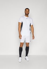 Weißes Sportoberteil mit schwarzen Seitenpaneelen, kombiniert mit weißen Shorts. Schwarze Socken und weiße Sportschuhe runden den sportlichen Look ab.