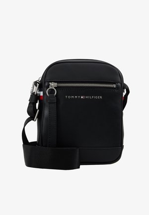 Sort Tommy Hilfiger crossbody taske med sølv lynlås, frontlogo, justerbar rem og rød-hvid-blåstribet detalje på siderne.