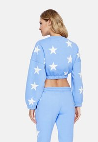 Felpa cropped azzurro chiaro con motivo a stelle bianche, dotata di maniche lunghe e vita elastica. Abbinata a pantaloni azzurro chiaro coordinati.