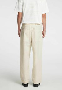 Jasnobeżowe spodnie z szerokimi nogawkami wykonane z miękkiego materiału, z tylnymi kieszeniami i luźnym krojem. Noszone z prostą białą koszulką.