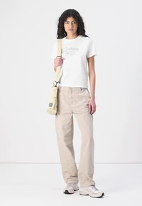 Hvit kortermet T-skjorte med "Carhartt WIP" tekst, beige vidbukser og en kremfarget crossbody-veske. Nøytrale sneakers fullfører antrekket.