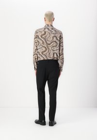 Lange mouwen shirt van een beige stof met een golvend bruin en zwart slangenpatroon. Gepaarde met zwarte broeken en zwarte schoenen.