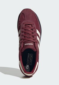 Maroon atletska cipela s gornjim dijelom od antilopa i tkanine, s bijelim prugama, vezanjem na vezice i crnom unutrašnjošću označenom kao "CLOUDFOAM COMFORT".