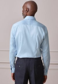 Šviesiai mėlyna ilgomis rankovėmis marškiniai su klasikiniu apykakliu ir sagų užsegamais rankogaliais, derinti su tamsiomis kelnėmis, kurios turi kišenes gale ir sagų detalės.