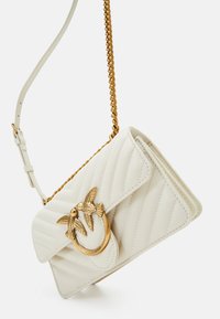 Borsa a mano in pelle bianca con design trapuntato, tracolla in catena dorata e un accento decorativo a forma di uccello nella parte anteriore.