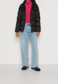 Doudoune noire, col roulé rose et jean bleu clair à coupe large avec ourlets effilochés. Chaussures noires complètent la tenue.