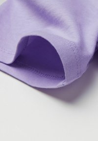 Tela de algodón lavanda con un primer plano detallado del borde de la manga doblada y dobladillada sobre un fondo blanco.