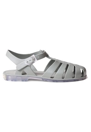 Sandale en plastique gris au design ouvert, comprenant plusieurs découpes, une bride ajustable et une semelle transparente. Ornée d'un logo sur le côté.