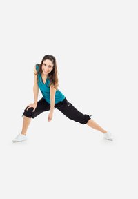 Outfit sportivo con un top aderente turchese e pantaloni neri a vita alta. Sneakers bianche, modello in una posa dinamica su uno sfondo neutro.