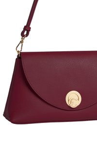 Borsa in pelle bordeaux con una texture liscia, forma triangolare, pattina curva e dettaglio della chiusura circolare in oro. Include una tracolla removibile.