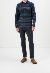 Navy button-up shirt with horizontal stripes, single chest pocket, paired with dark pants and brown slip-on shoes. Smooth texture.