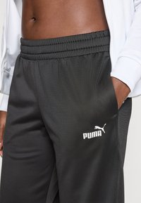 Svarta träningsbyxor med elastisk midja, sidoficka och vit Puma-logotyp på nedre vänstra benet. Slät, lättviktsmaterial.
