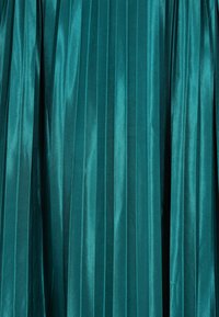 Türkiz, pliszírozott anyag fényes felülettel és függőleges csíkmintával, sima textúrával és gazdag színmélységgel.