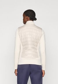 Ljusgrön zip-up väst med kviltad textur på baksidan, med hög krage och strukturerad passform. Matchad med marinblå byxor.