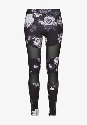 Leggings de sport noirs avec un motif floral blanc, dotés de panneaux en maille transparente et d'une coupe ajustée. Tissu doux au toucher lisse.