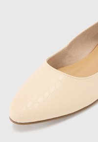 Pointed-toe flat in light beige, made of textured faux leather. Features a smooth inner lining and a low, brown outsole.