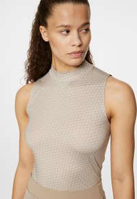 Top senza maniche beige con colletto alto, caratterizzato da un motivo geometrico testurizzato. Tessuto liscio, design aderente, estetica minimalista.