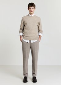 Beiger Strickpullover kombiniert mit einem weißen Hemd mit Kragen, hellgrauer, maßgeschneiderter Hose und dunklen Schuhen, mit schlichtem Design und klaren Linien.