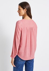 Blusa rosa chiaro a maniche lunghe con dettagli arricciati sul retro, orlo arrotondato e polsini con bottoni, realizzata in un tessuto morbido.