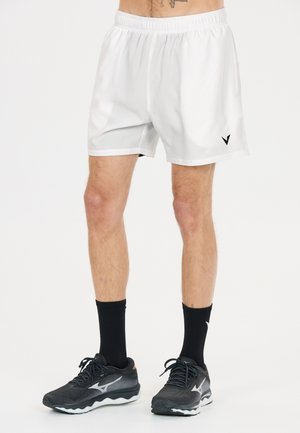 Mannelijke benen met witte sportshorts, zwarte kousen en zwarte hardloopschoenen met witte zolen op een witte achtergrond.
