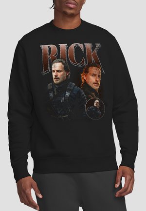 Man wearing black sweatshirt with three portraits of a bearded man in tactical gear and large text reading "RICK" on front.