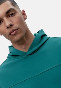 Mäta zelená mikina s kapucňou vyrobená z hladkej tkaniny, s minimalistickým dizajnom a jemným textúrovaným panelom cez hruď.