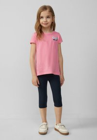 T-shirt rose à manches courtes avec broderie florale sur la poitrine, associé à des leggings capri bleu marine et des baskets blanches avec des semelles marron clair.