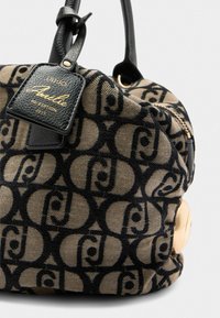 Sac en toile avec un motif brun et noir, doté d'une étiquette en cuir, de quincaillerie dorée et d'une silhouette arrondie.