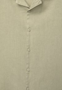 Chemise en lin beige clair vue de face avec col et cinq boutons ronds visibles disposés en rangée verticale.